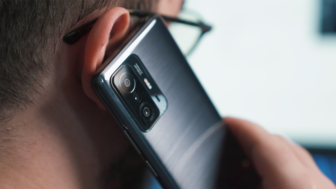 Person wearing glasses makes a call on a dark grey smartphone.